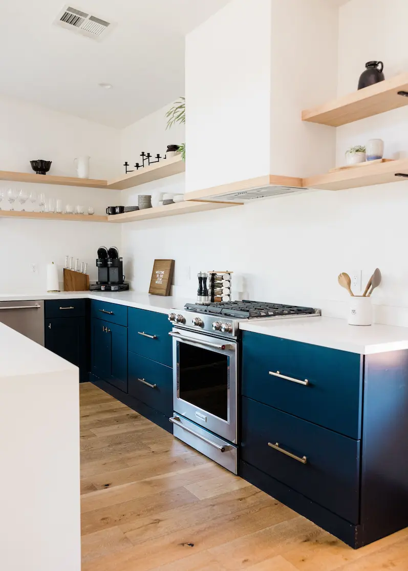 Moderne Küchenrenovierung mit Holzboden, dunkelblauen Unterschränken und offenen Holzregalen in einer Ferienwohnung auf Mallorca